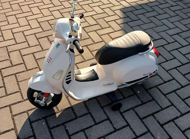 Baltas vaikiškas Vespa tipo elektrinis motociklas ant trinkelių